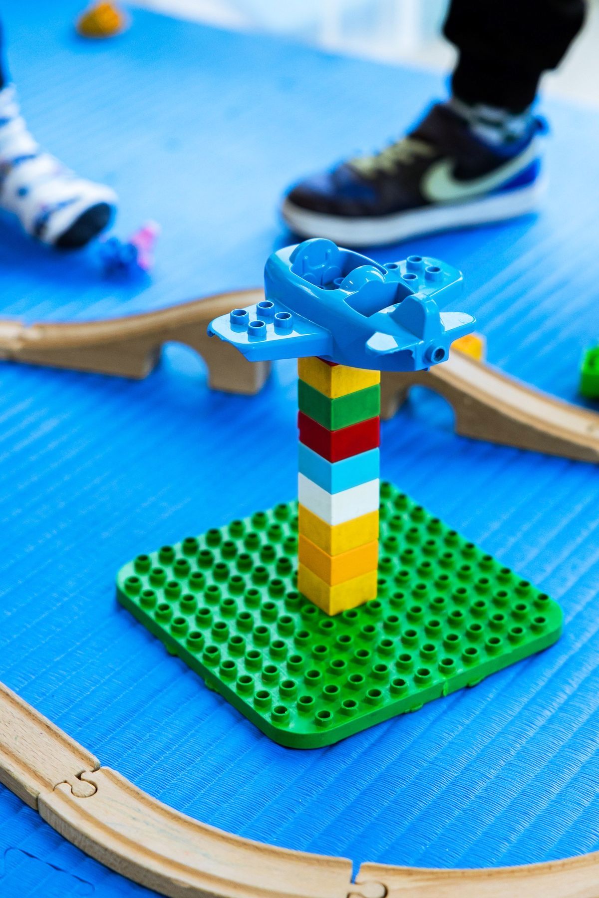 Una torre di mattoncini colorati con un aeroplano blu in cima, fra i binari di legno su un tappeto blu